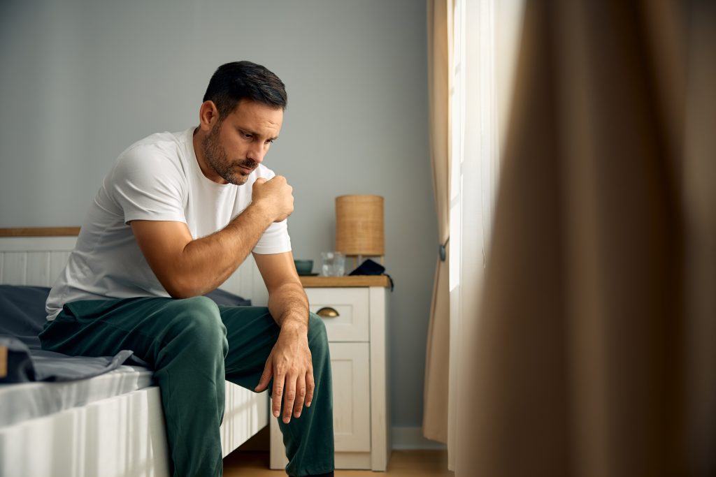 Mid adult man coping with depression while sitting alone in the morning in bedroom.