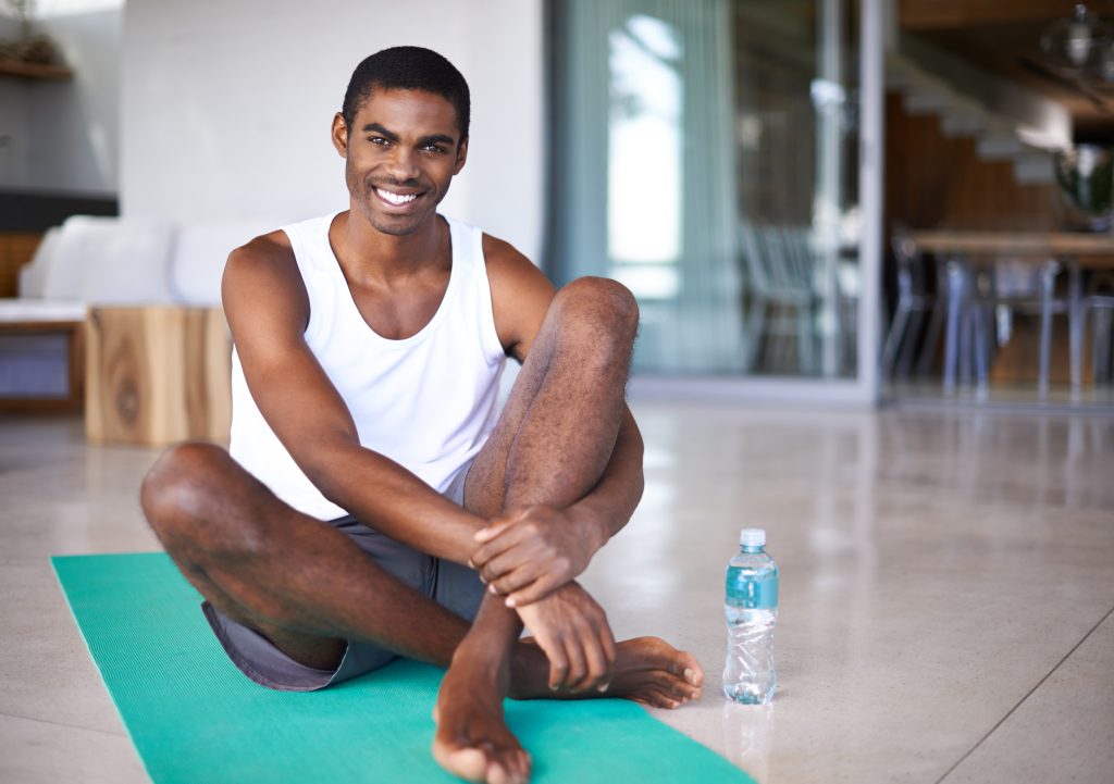 A man sits on a yoga mat, holding a water bottle, preparing for his yoga practice for Managing Opioid Dependence.