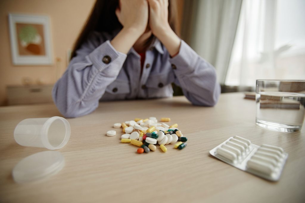 Pile of pills and tablets in table with young woman stressed.