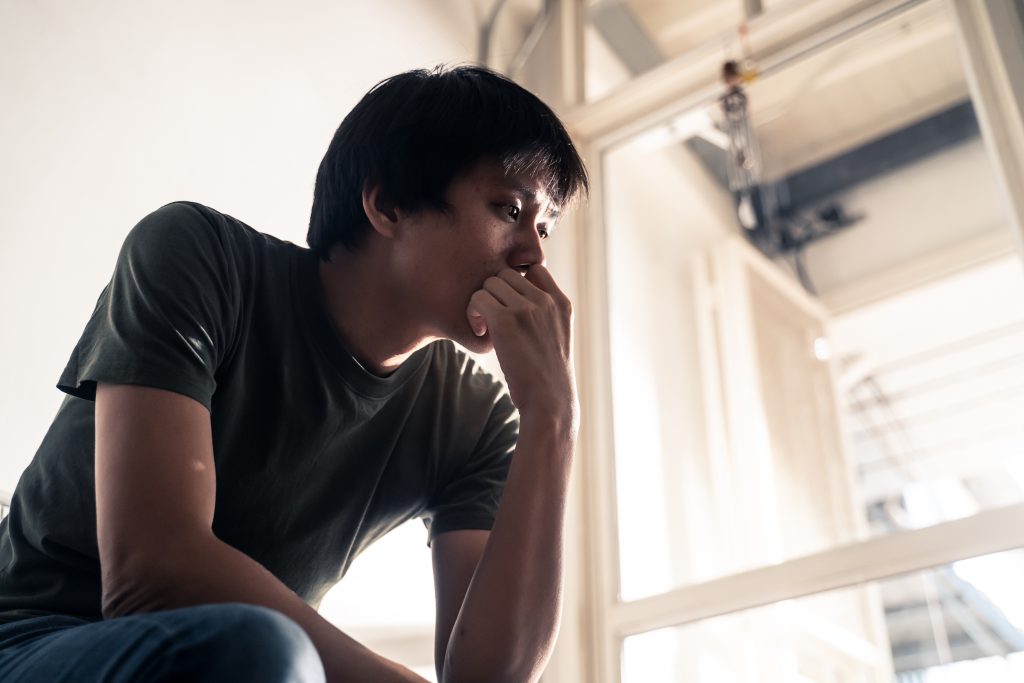 A man sitting on the floor, resting his chin on his hand, appears deep in thought.
