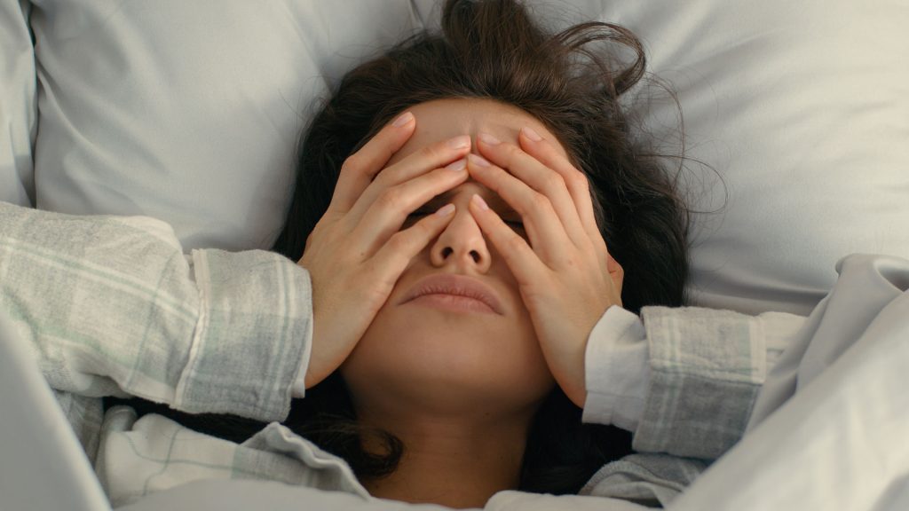 A stressed woman in bed grabbing her face.