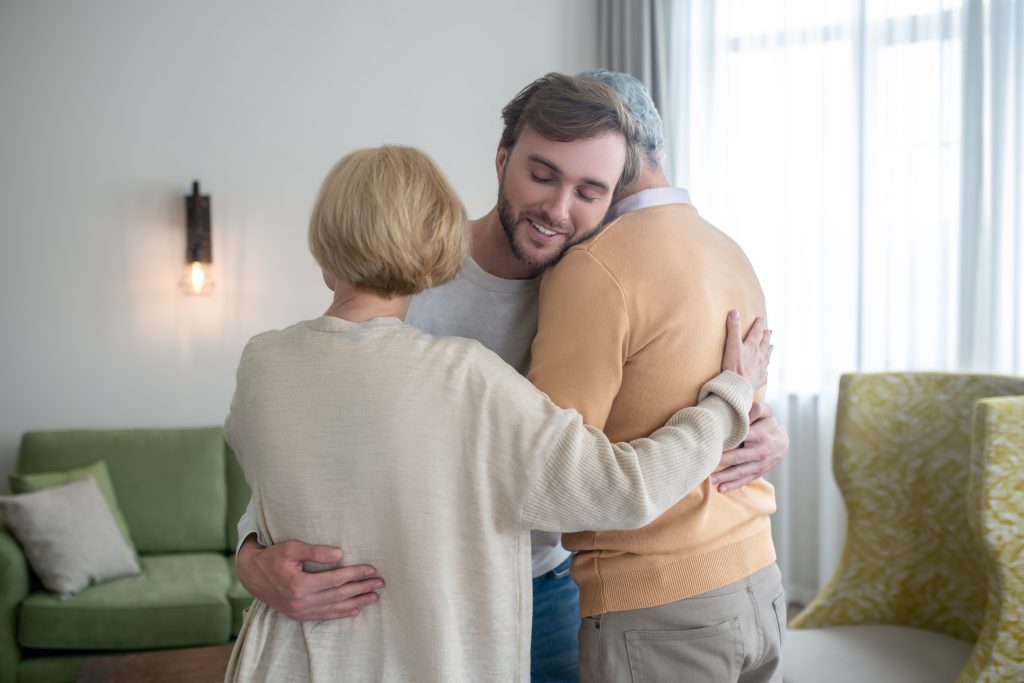 A man and woman embrace affectionately in a cozy living room filled with warm lighting and comfortable furniture.