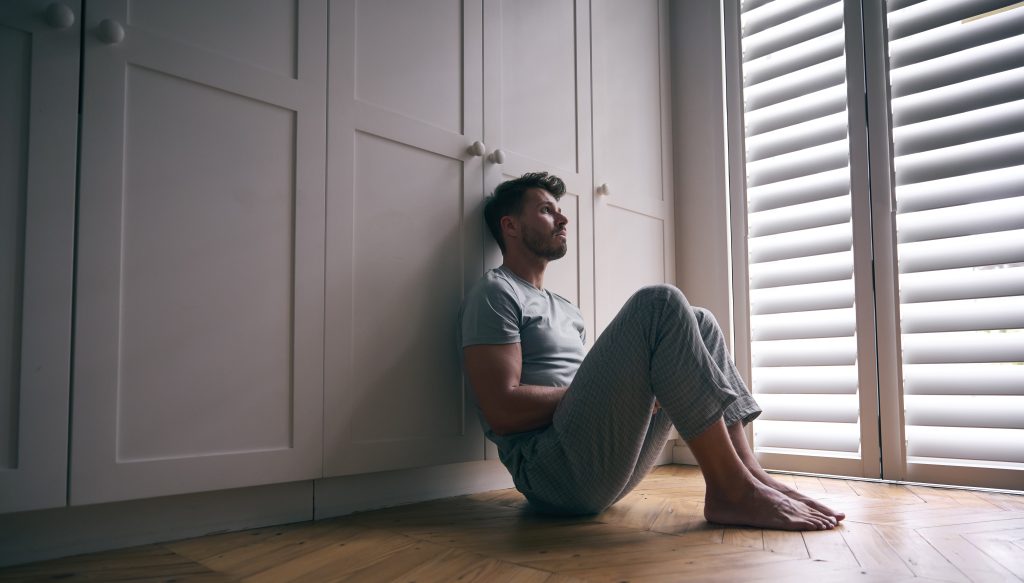 A man sitting on the floor in front of a white cabinet, looking relaxed, contemplative and trying on Quitting marijuana dependency.