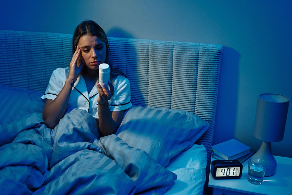 Woman with insomnia and anxiety looking at a bottle of pills.