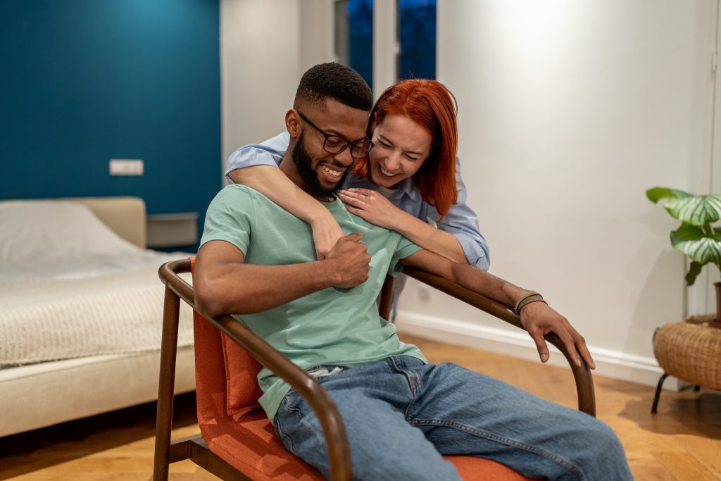 A man and woman sitting together on a chair in a cozy bedroom, surrounded by soft lighting and warm decor Overcoming Sedative Addiction.