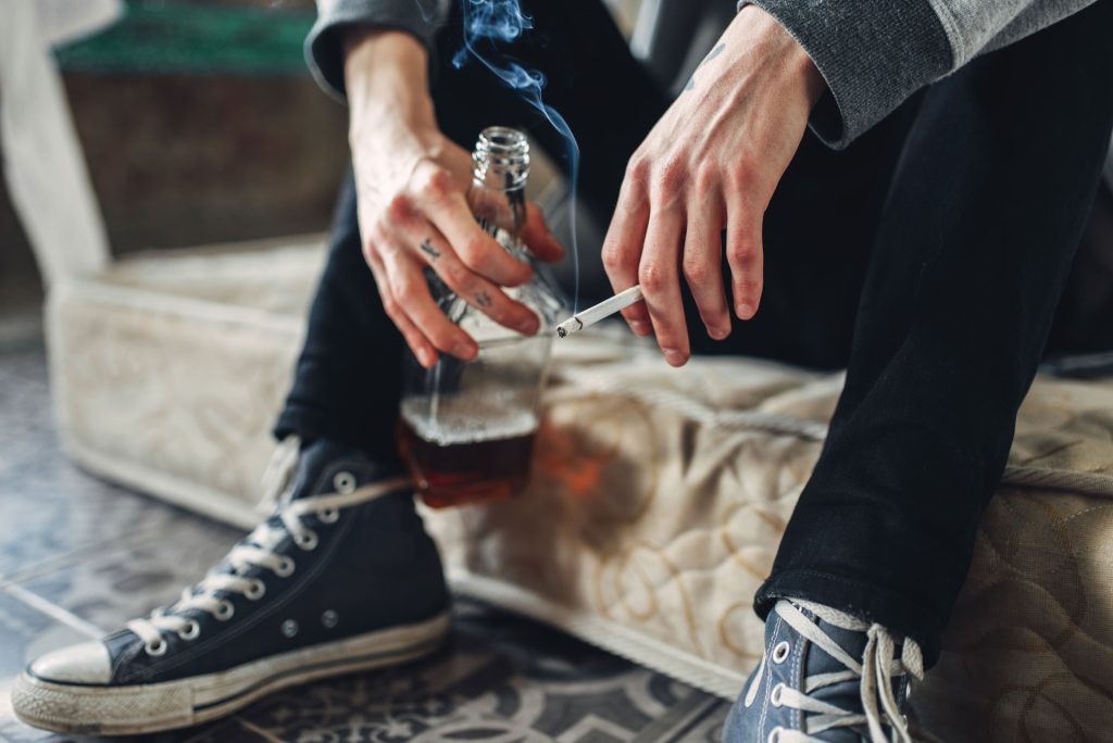 Cropped photo of a male with substance abuse drinking alcohol and smoking ciggarette.
