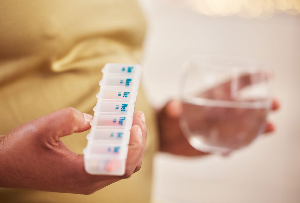 Woman holding a glass of water and pill organizer.