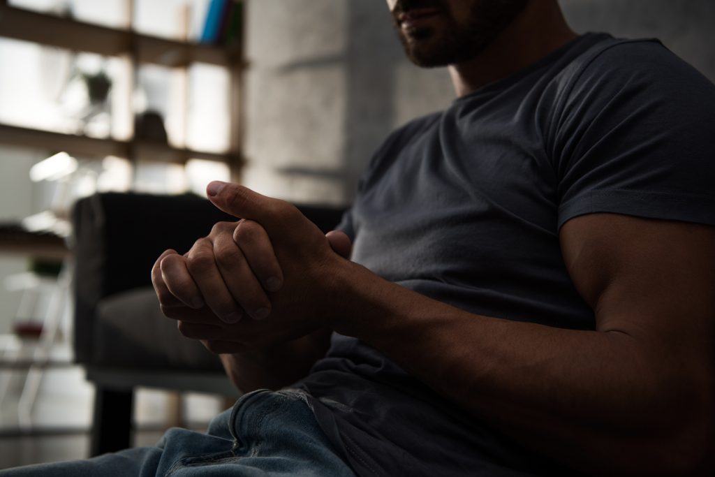 A man sits on a couch with his arms crossed, looking thoughtfully ahead.