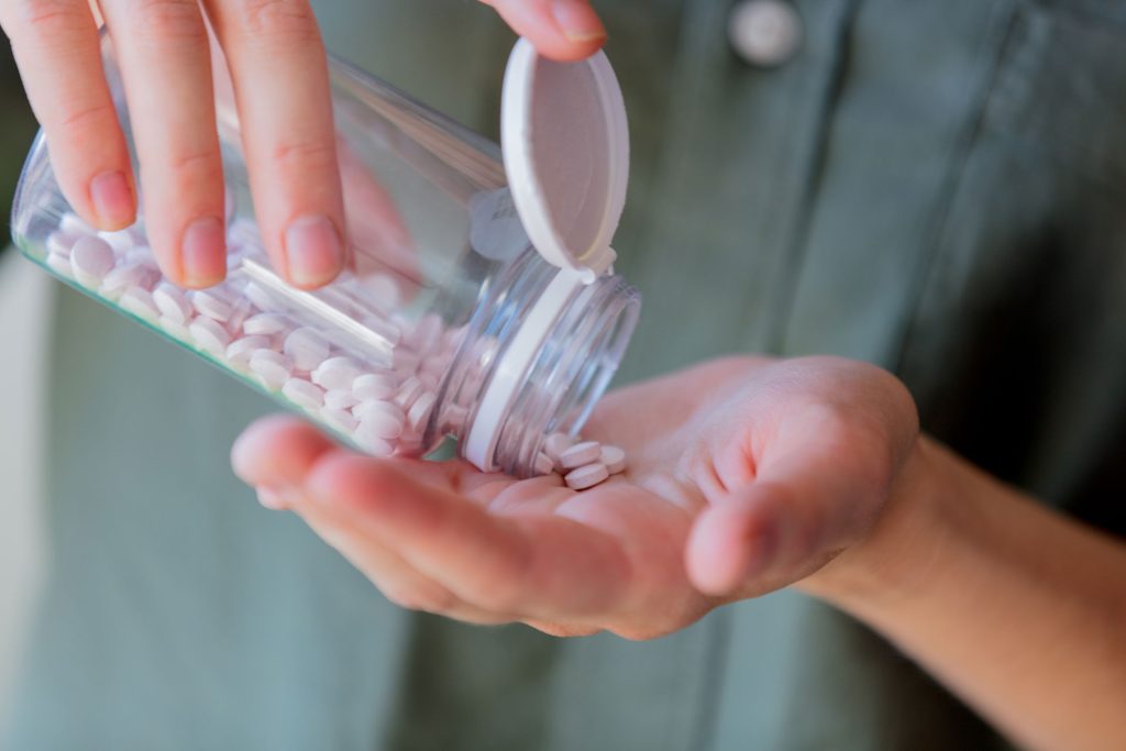 Woman pours white pills from a jar.