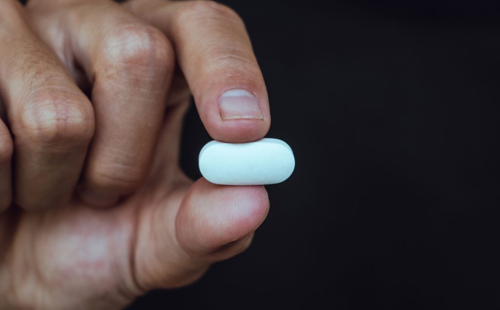 Human hand holding white pill.