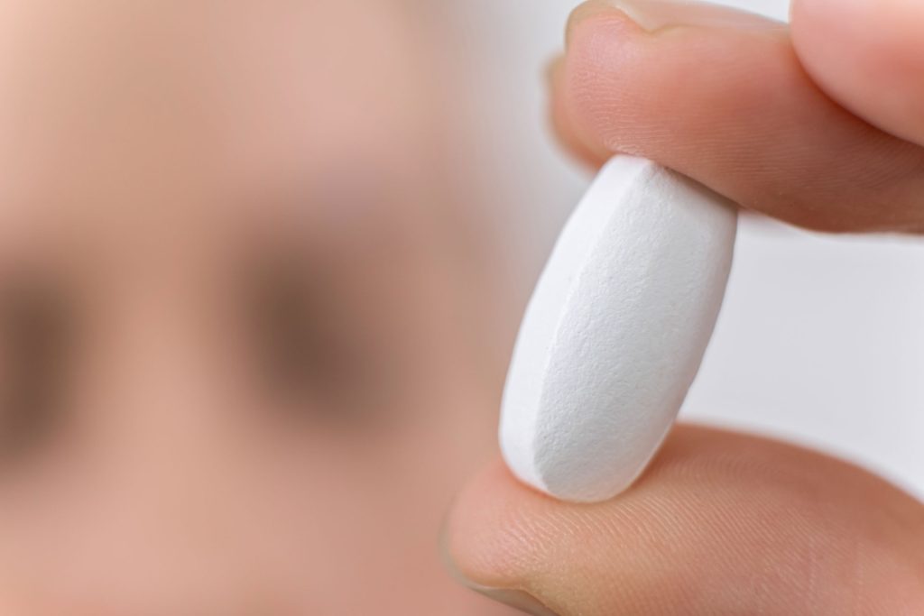 Hand holding a white pill.